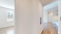 Located in Port Royal, SC, this single-floor, 2-bedroom, 1-bathroom home offers a clean, modern aesthetic throughout. Light wood-tone flooring runs consistently across all rooms, complemented by crisp white walls and white trim that create a bright, cohesive atmosphere.

The open living area is bathed in natural light streaming through sliding glass doors that lead to a balcony, with a ceiling fan overhead adding to the airy feel. The hallway features a built-in utility panel, providing practical convenience near the entry.

The kitchen is a standout feature, showcasing granite countertops, a large center island with an undermount sink, taupe flat-front cabinetry, a white subway tile backsplash, and a full suite of stainless steel appliances including a refrigerator with ice maker, range, and microwave. Pendant lighting above the island adds a refined touch.

The spacious primary bedroom is filled with natural light from multiple windows fitted with blinds, and includes a ceiling fan and closet access. The second bedroom also benefits from natural light through corner windows.

The bathroom is well-finished with granite countertops, a single undermount sink, taupe cabinetry, a large mirror, built-in shelving, and a glass-enclosed shower.