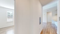 Located in Port Royal, SC, this single-floor, 2-bedroom, 1-bathroom home offers a clean, modern aesthetic throughout. Light wood-tone flooring runs consistently across all rooms, complemented by crisp white walls and white trim that create a bright, cohesive atmosphere.

The open living area is bathed in natural light streaming through sliding glass doors that lead to a balcony, with a ceiling fan overhead adding to the airy feel. The hallway features a built-in utility panel, providing practical convenience near the entry.

The kitchen is a standout feature, showcasing granite countertops, a large center island with an undermount sink, taupe flat-front cabinetry, a white subway tile backsplash, and a full suite of stainless steel appliances including a refrigerator with ice maker, range, and microwave. Pendant lighting above the island adds a refined touch.

The spacious primary bedroom is filled with natural light from multiple windows fitted with blinds, and includes a ceiling fan and closet access. The second bedroom also benefits from natural light through corner windows.

The bathroom is well-finished with granite countertops, a single undermount sink, taupe cabinetry, a large mirror, built-in shelving, and a glass-enclosed shower.
