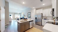 Located at 4040 Candleberry Gdn in North Augusta, SC, this single-story home combines modern finishes with a warm, welcoming design throughout. The open-concept kitchen is a standout feature, showcasing white shaker cabinetry, a classic subway tile backsplash, quartz countertops, a central island with an undermount sink, and a full suite of stainless steel appliances. The kitchen flows seamlessly into the living area, where vaulted ceilings and generous windows invite abundant natural light, creating an airy and expansive feel. The living room offers a comfortable layout ideal for relaxing or entertaining. The primary bedroom is generously proportioned, featuring a tray ceiling with a ceiling fan and multiple windows that bring in outdoor views and natural light. The en-suite bathroom is well-appointed with a dual-sink vanity, white cabinetry, quartz countertops, and hardwood-style flooring. A central hallway connects the remaining rooms, with additional bathroom access visible from the corridor. Hardwood-style flooring runs throughout the home, lending continuity and warmth. The exterior features a pool and a well-maintained yard, as visible in the aerial view, rounding out this thoughtfully designed residence.