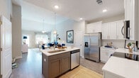 Located at 4040 Candleberry Gdn in North Augusta, SC, this single-story home combines modern finishes with a warm, welcoming design throughout. The open-concept kitchen is a standout feature, showcasing white shaker cabinetry, a classic subway tile backsplash, quartz countertops, a central island with an undermount sink, and a full suite of stainless steel appliances. The kitchen flows seamlessly into the living area, where vaulted ceilings and generous windows invite abundant natural light, creating an airy and expansive feel. The living room offers a comfortable layout ideal for relaxing or entertaining. The primary bedroom is generously proportioned, featuring a tray ceiling with a ceiling fan and multiple windows that bring in outdoor views and natural light. The en-suite bathroom is well-appointed with a dual-sink vanity, white cabinetry, quartz countertops, and hardwood-style flooring. A central hallway connects the remaining rooms, with additional bathroom access visible from the corridor. Hardwood-style flooring runs throughout the home, lending continuity and warmth. The exterior features a pool and a well-maintained yard, as visible in the aerial view, rounding out this thoughtfully designed residence.