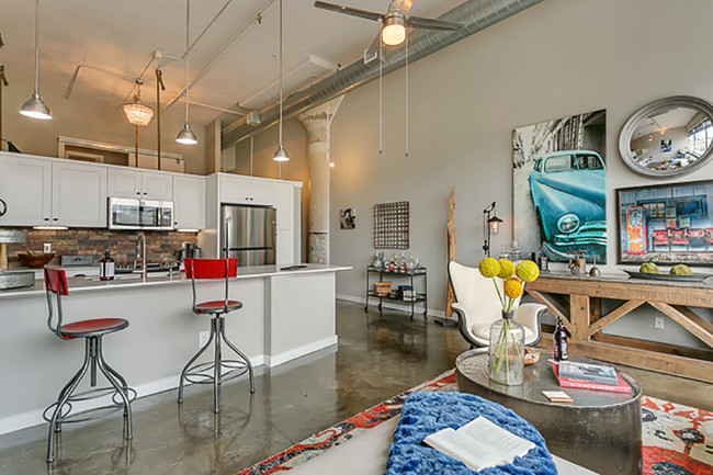 Living room with open concept kitchen, concrete floor, and beautiful white cabinets. Loft style apartment - Lofts at Mockingbird Station Apartments