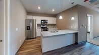 This single-floor residence at 2827 Rupp Dr in Fort Wayne, Indiana offers a well-designed layout with a neutral, contemporary aesthetic throughout. The kitchen is a standout feature, equipped with white shaker-style cabinetry, granite countertops, and a full suite of stainless steel appliances including a side-by-side refrigerator with ice and water dispenser, electric range, over-the-range microwave, and dishwasher. A peninsula island with an undermount sink and pendant lighting above adds both function and style, while wood-look vinyl plank flooring ties the kitchen and adjacent living areas together seamlessly. The living area is generously proportioned, featuring a ceiling fan, multiple tall windows that allow ample natural light, and a combination of wood-look flooring and plush carpet. The bedrooms are carpeted for comfort, with neutral-toned walls, good-sized windows with blinds, and adequate closet space. One room features a transitional flooring detail, blending carpet and vinyl plank. The bathroom is finished with a walk-in shower, granite-topped vanity with white cabinetry, and wood-look flooring. Throughout the unit, consistent dark baseboards, taupe wall tones, and recessed and flush-mount lighting contribute to a clean, cohesive interior.