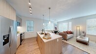 This well-appointed single-floor residence showcases a thoughtfully designed open-concept layout that seamlessly connects the kitchen, dining, and living areas. The kitchen is a standout feature, equipped with stainless steel appliances including a French door refrigerator, electric range, and over-the-range microwave. Light wood-grain cabinetry, a tile backsplash, and a large center island with a white quartz countertop and integrated sink anchor the space. Pendant lighting and track lighting add warmth and functionality overhead.

The living area is bright and airy, with multiple large windows fitted with horizontal blinds that allow for generous natural light while maintaining privacy. Wood-look flooring runs throughout the main living spaces and hallway, lending a cohesive and contemporary feel.

A clean, well-lit hallway connects the private quarters, where the bedroom offers a comfortable retreat with a closet and natural light from a window with sheer curtains. Both bathrooms feature marble-style tile flooring and tub surrounds, floating wood-tone vanities, and white quartz countertops. The primary bathroom includes direct access to a walk-in closet. The second bathroom is equally refined, with a tub-shower combination and coordinating finishes, maintaining the modern aesthetic found throughout the entire residence.