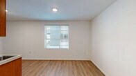 This efficiently designed single-floor studio at 5210 makes smart use of its compact footprint, offering a well-organized layout that includes a living area, kitchenette, and a full bathroom. The interior is finished with warm wood-look luxury vinyl flooring throughout, lending a cohesive and modern feel to the entire space.

The main living area is bright and open, featuring a window fitted with horizontal blinds that allows natural light to filter in while maintaining privacy. Clean white walls and recessed lighting contribute to an airy, uncluttered atmosphere.

The kitchenette is thoughtfully appointed with warm-toned wooden cabinetry — both upper and lower — providing ample storage. It is equipped with a stainless steel sink, a compact refrigerator, and a microwave, making it fully functional for everyday use. Built-in shelving nearby offers additional organizational space.

The bathroom is neatly laid out, featuring a vanity with wooden cabinetry, a toilet, and a walk-in shower stall. Consistent with the rest of the unit, wood-look flooring extends into the bathroom, reinforcing the space's unified design language.

Overall, this studio presents a clean, contemporary living environment with practical amenities, making it a well-suited option for those seeking a streamlined and low-maintenance space.