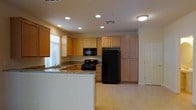 This two-story home offers a functional and inviting layout designed for comfortable everyday living. The kitchen serves as a central highlight, featuring light maple cabinetry that extends to the ceiling, providing generous storage throughout. Granite-style countertops add a touch of elegance, while black appliances — including a gas range, built-in microwave, and a full-sized refrigerator — offer a cohesive, modern aesthetic. A peninsula counter extends into the space, creating a natural divide between the kitchen and the adjoining area, and offering additional prep or casual dining space. Recessed lighting throughout the kitchen ensures bright, even illumination, complementing the natural light that filters in through a window above the sink. The light-toned tile flooring unifies the space and contributes to an open, airy feel. A doorway visible from the kitchen hints at additional rooms beyond, suggesting a well-connected floor plan. The overall design balances practicality with a clean, neutral palette, making it a versatile space suited to a variety of lifestyles across both floors of the home.