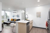 This thoughtfully designed single-floor unit offers a clean, contemporary aesthetic with light wood flooring and bright white walls throughout. The open-concept kitchen flows seamlessly into the living area, anchored by a light wood island with a white quartz countertop, pendant lighting, stainless steel appliances — including a refrigerator, range, and built-in microwave — and ample cabinetry. The adjoining living space benefits from large windows that invite generous natural light and offer views of surrounding greenery and the urban skyline beyond. A wall-mounted mini-split system provides climate control throughout the unit. The entry foyer is practical and welcoming, featuring a louvered closet and a small decorative shelf. Multiple bedrooms are present, each with light wood flooring, large windows that frame outdoor views, and dedicated workspace areas. Select bedrooms feature ceiling fans and roller shade window treatments. The bathrooms are finished to a high standard, showcasing light wood vanities with marble-style quartz countertops, undermount sinks, matte black fixtures, oversized mirrors, and a tub-shower combination enclosed by sliding glass doors with black framing. The overall ambiance is modern, bright, and functional.