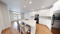 Located at 8496 Phelan Blvd in Beaumont, TX, this thoughtfully designed one-bedroom, one-bathroom unit offers a clean, modern aesthetic throughout its single floor. The open-concept layout centers around a well-appointed kitchen featuring crisp white cabinetry, a subway tile backsplash, white quartz countertops, and a central island with a built-in sink and seating for two — ideal for casual dining or entertaining. Black appliances, including a range, microwave, and refrigerator, provide a bold contrast to the bright white finishes. Recessed lighting and warm hardwood-style flooring flow seamlessly throughout the main living area, which is bathed in natural light from French doors leading to the exterior. Built-in open shelving adds practical storage and character to the living space. The bedroom is a comfortable, light-filled room with a ceiling fan, window with outdoor views, and easy access to the full bathroom. The bathroom features a modern floating vanity with ample drawer storage, white countertops, and a tiled walk-in shower. A dedicated walk-in closet provides generous storage. The unit's clean lines, neutral palette, and efficient use of space create a bright and welcoming atmosphere throughout.