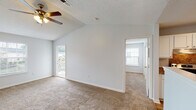This single-floor residence at 2920 Cosmo Pl in Fayetteville, NC offers a well-designed layout with a variety of comfortable living spaces. The living area is generously sized, featuring vaulted ceilings, plush wall-to-wall carpeting, and a ceiling fan with light fixture. Natural light flows in through multiple windows fitted with blinds, and a sliding door provides direct access to a private balcony with outdoor views. The open layout connects the living area seamlessly to the kitchen, which is equipped with white cabinetry, stone-look countertops, a double-basin sink, stainless steel appliances including an electric range and refrigerator, and a decorative tile backsplash. Hardwood-style flooring runs through the kitchen and adjoining areas. The bedrooms are carpeted and well-lit, each featuring ceiling fans, ample natural light from windows with blinds, and closet space. The bathroom includes a full tub and shower surround with clean, neutral finishes. Throughout the residence, the textured ceilings, neutral wall tones, and consistent design elements create a cohesive and inviting atmosphere suited for comfortable everyday living.