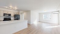 This thoughtfully designed 2-bedroom, 1-bathroom single-floor home offers a clean, modern aesthetic with a bright and open feel throughout. Light wood-tone flooring runs through the main living areas, complementing the crisp white walls and abundant natural light that streams in through vertical-blind-covered windows.

The open-concept living area flows seamlessly from the kitchen, which features a peninsula with white countertops, wood-tone cabinetry, and black appliances including a full-size refrigerator and range. A window in the kitchen adds additional natural light to the space.

The living room is generously proportioned, offering an airy, versatile layout. Both bedrooms are well-sized and bright, each with a window and wall-mounted mini-split HVAC unit for individual climate control. The primary bedroom is a comfortable size, while the second bedroom features soft carpet flooring and a sliding-door closet with wire shelving for ample storage.

The full bathroom includes a tub/shower combination with clean white surrounds and light wood-tone flooring. A dedicated laundry room houses a full-size washer and dryer with overhead wire shelving, adding great convenience. The overall ambiance is clean, modern, and move-in ready.