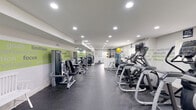 Located at 4217 Chapel Rd in Perry Hall, Maryland, this fitness facility offers a thoughtfully designed workout environment spread across a single floor. The space is organized to accommodate a wide variety of training styles, with clearly defined areas for both cardiovascular and strength-based exercise.

The main workout area is generously proportioned, featuring a row of Matrix cardio machines including treadmills, ellipticals, and stair climbers positioned along one side of the room. Opposite these, a selection of Matrix strength training machines provides options for targeted muscle conditioning. A functional trainer cable machine anchors a dedicated strength zone, accompanied by free weights and benches for versatile training.

The interior design is clean and modern, with white and grey walls adorned with motivational fitness-themed typography in green and white, creating an energizing atmosphere. Durable rubberized flooring runs throughout, offering both safety and comfort. Recessed lighting illuminates the space evenly, maintaining a bright and welcoming environment.

A water cooler station is conveniently positioned within the facility, and wall-mounted televisions provide entertainment during cardio sessions. Natural light filters in through windows with blinds, and a wall-mounted HVAC unit ensures climate comfort year-round. Signage reminding users to clean equipment after use reflects a commitment to cleanliness and community standards.