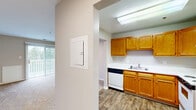 Located at Kings Crest Court in Fredericksburg, Virginia, this two-bedroom, one-bathroom unit offers a practical and well-organized single-floor layout. The kitchen is equipped with warm honey-toned wood cabinetry, white appliances including a range, refrigerator, and dishwasher, along with a double sink and wood-look flooring that adds a clean, durable finish. A hallway connects the main living areas, and a balcony provides an outdoor retreat with views of the surrounding greenery. The living room features carpeted flooring and access to natural light through sliding balcony doors. Both bedrooms are carpeted and finished in neutral tones, each offering windows that bring in natural light and views of the neighborhood. The primary bedroom includes its own dedicated closet, while additional closets throughout the unit provide generous storage. A total of three closets ensures ample organization space. The bathroom features a walk-in shower with white tile surround, a beige accent stripe, and wood-look flooring complementing the vanity cabinetry. The overall aesthetic throughout the unit is clean and neutral, with textured ceilings, white trim, and a consistent warm-toned palette creating a cohesive and move-in-ready atmosphere.