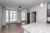 This single-floor unit showcases a thoughtfully designed open-concept layout that seamlessly connects the kitchen and living area. The kitchen is well-appointed with dark espresso cabinetry contrasted by a white subway tile backsplash, granite countertops, and a full suite of stainless steel appliances, including a range, microwave, dishwasher, and refrigerator. A central granite-topped island provides additional prep space and serves as a natural divider between the kitchen and the living area, with a globe pendant light overhead adding a modern touch.

The living area is bright and airy, benefiting from multiple windows fitted with horizontal blinds that allow natural light to filter through. A ceiling fan enhances comfort, while light hardwood flooring runs consistently throughout the space, lending warmth and continuity. Neutral gray walls keep the aesthetic clean and versatile.

A dedicated laundry closet houses a stacked washer and dryer unit alongside wall-mounted shelving for storage convenience. The bathroom features a tub-shower combination with chrome fixtures, a vanity with a granite countertop, and light hardwood flooring that mirrors the rest of the unit. A hallway connects the bathroom to the remaining rooms, completing this efficiently arranged and modern living space.