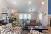 Located at 1543 Ambergrove Dr in San Jose, CA, this single-floor space offers an open, airy layout enhanced by dramatic vaulted ceilings that lend a sense of generous vertical space throughout. The living area serves as the focal point of the home, anchored by a classic tile-surround fireplace and a soaring accent wall painted in a rich teal blue, adding a bold yet inviting splash of color. Warm hardwood-style flooring runs throughout, unifying the open-plan interior.

Pendant light fixtures hang elegantly from the high ceiling, casting a warm glow over both the living and dining areas. The dining space accommodates a full table and chairs, bathed in natural light streaming through vertical blinds that cover large windows and a sliding glass door. The slider opens to an outdoor view of a sparkling community pool, bringing a resort-like ambiance directly into the space.

A structural column and open passageway define the transition between zones without sacrificing the sense of openness. Additional highlights include a tiled entry area, a decorative rock garden inset, and a well-placed mirror that amplifies the natural light. HVAC vents integrated into the ceiling ensure year-round comfort. The overall ambiance is warm, open, and welcoming, blending casual comfort with distinctive architectural character.