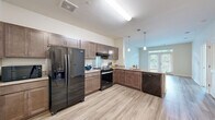 Located at 400 Katrina Ct in Midlothian, VA, this single-floor residence offers a thoughtfully designed layout that maximizes functionality and comfort. The open-concept kitchen and living area serves as the heart of the home, featuring rich wood-toned cabinetry, granite countertops, a large peninsula with pendant lighting, and a full suite of black stainless steel appliances including a side-by-side refrigerator, range, and dishwasher. Light wood-style flooring runs throughout the main living areas, enhancing the bright, airy atmosphere. The living room is anchored by elegant French doors with transom windows above, allowing generous natural light to fill the space and providing access to an outdoor area. The bedroom is carpeted for comfort and features corner windows with wooded views, flooding the room with soft, natural light. A spacious walk-in closet with wire shelving provides ample storage. The bathroom includes a tub-shower combination. Additional practical spaces include a pantry, laundry area, and utility rooms, ensuring all household needs are efficiently accommodated within this well-organized, move-in-ready residence.