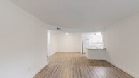 This single-floor unit presents a clean, modern aesthetic throughout, unified by light wood-style flooring and crisp white walls. The open-concept living and dining area is generously proportioned, flowing seamlessly toward the kitchen peninsula, which features a built-in sink and granite-style countertops — an ideal spot for casual dining or meal prep. The galley kitchen is well-appointed with white cabinetry extending to the ceiling, matching granite-style countertops along both walls, a double stainless steel sink, and a full suite of white appliances including a refrigerator, electric range, and built-in microwave.

The unit includes two bedrooms, each benefiting from natural light through large windows with exterior views of mature trees and surrounding greenery. One bedroom features mirrored sliding closet doors with interior shelving. Both rooms offer a calm, neutral atmosphere well-suited to a variety of uses.

Two bathrooms serve the unit: one with a tub-shower combination and a granite-topped vanity, and a second featuring a walk-in shower with mosaic tile flooring and an equally refined vanity. Throughout, the consistent use of white finishes, light flooring, and recessed and flush-mount lighting creates a bright, cohesive living environment.