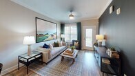 This single-floor residence is thoughtfully designed with a cohesive, contemporary aesthetic carried throughout its living spaces. The open-concept living and dining area serves as the heart of the unit, featuring wood-look plank flooring, crown molding, and neutral warm-toned walls. The living room offers access to a private balcony through a glass-paneled door, allowing natural light to fill the space, while a bold dark accent wall adds visual depth. The dining area sits adjacent, providing a natural flow between spaces.

The kitchen is well-equipped with white shaker-style cabinetry, granite countertops, a classic subway tile backsplash, and a full suite of stainless steel appliances, including a refrigerator, range, microwave, and dishwasher. A breakfast bar with seating connects the kitchen to the main living area.

The primary bedroom features a teal accent wall, a ceiling fan, a generous window with exterior views, and access to an en suite bathroom appointed with a dual-sink vanity, granite countertops, gray shaker cabinets, and dual framed mirrors with a brushed nickel light bar. A second bedroom offers comparable comfort, also with a ceiling fan. The second bathroom includes a full tub-shower combination with tile surround.