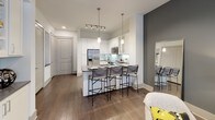 This 1-bedroom, 1-bathroom residence is designed with a clean, contemporary aesthetic that balances style and functionality across a single floor. The open-concept living and kitchen area serves as the heart of the home, featuring rich hardwood-style flooring, recessed track lighting, and a striking accent wall in a deep slate-gray tone that adds depth and contrast to the bright, neutral palette.

The kitchen is a standout feature, outfitted with crisp white shaker cabinetry, a classic subway tile backsplash, and dark gray countertops. Stainless steel appliances — including a range, microwave, refrigerator, and dishwasher — deliver a polished, modern look. Pendant lighting illuminates the breakfast bar peninsula, which offers seating and a natural transition into the living area.

The bedroom is a comfortable retreat, complete with a ceiling fan, large windows that invite natural light, and direct access to a closet. The room's neutral tones and clean lines create a calm, restful atmosphere.

The bathroom is finished in an all-white palette, featuring a shaker-style vanity with an undermount sink, a large mirror, chrome fixtures, and built-in open shelving above the toilet for practical storage. The overall design of this residence is cohesive, modern, and move-in ready.