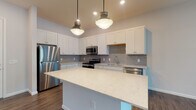 Located at 20 Olentangy Meadows Dr in Lewis Center, Ohio, this single-floor unit offers a well-designed, modern layout with thoughtful finishes throughout. The open-concept kitchen serves as the heart of the home, showcasing crisp white shaker cabinetry, a classic gray subway tile backsplash, and a generous center island topped with light quartz countertops featuring subtle veining. A full suite of stainless steel appliances — including a refrigerator, range, microwave, and dishwasher — completes the kitchen, which is illuminated by stylish pendant lighting and recessed fixtures. Dark hardwood-style flooring runs through the main living and kitchen areas, providing a warm contrast to the bright, neutral walls. The living area is spacious and filled with natural light through multiple windows dressed with clean white blinds, offering views of the surrounding greenery. Bedrooms feature plush neutral carpeting and natural light from well-placed windows. The bathroom is finished with white cabinetry, a broad vanity mirror with bold dark framing, and hardwood-style flooring, with access to a walk-in closet complete with built-in shelving. Throughout the unit, tall ceilings and a clean, contemporary palette create an airy and inviting atmosphere.
