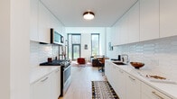 Located at 845 W Madison St in Chicago's vibrant West Loop neighborhood, this single-floor unit delivers a clean, contemporary design with an open, efficient layout. The galley-style kitchen runs along both walls, outfitted with white flat-front cabinetry extending to the ceiling, stainless steel appliances including a gas range and built-in microwave, a deep undermount sink, and a distinctive hexagonal white tile backsplash. Light wood-tone flooring flows continuously throughout, reinforcing a cohesive, modern aesthetic.

The living area benefits from tall, floor-to-ceiling windows framed in matte black that flood the space with natural light and provide views of the surrounding greenery and cityscape. The open connection between the kitchen and living area creates a functional, airy feel suited to everyday living and entertaining.

The bedroom is well-proportioned, featuring its own large black-framed window with outdoor views, and light-filled white walls that complement the wood flooring. The bathroom is finished with large-format floor tile, a white vanity with an integrated sink, a framed mirror with a dark border, and vertically stacked white wall tile. The entry corridor provides a clean transition into the unit, with additional storage integrated along the kitchen wall.