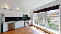 Located at 1525 NW 23rd Ave in Portland's vibrant Northwest District, this modern single-floor unit offers a clean, contemporary design throughout. Warm hardwood flooring extends across the open living and kitchen areas, creating a cohesive and inviting atmosphere. The open-concept living space is highlighted by a soothing teal accent wall and a large picture window that frames lush greenery outside, flooding the room with natural light. A wall-mounted mini-split system provides efficient climate control. The kitchen is well-appointed with sleek white flat-front cabinetry reaching to the ceiling, a bold black subway tile backsplash, light stone countertops, and a full suite of stainless steel appliances including a refrigerator, range, microwave, and dishwasher. A recessed sliding door reveals a dedicated laundry closet with a stacked washer and dryer, adding everyday convenience. The bathroom features a clean, all-white finish with tile flooring, a tub-shower combination, a vanity with integrated sink, and a large mirror. Recessed lighting throughout maintains a bright and polished aesthetic. The thoughtful layout and modern finishes make this a functional and stylish space in one of Portland's most walkable neighborhoods.