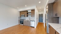 This well-appointed one-bedroom, one-bathroom residence offers a thoughtfully designed single-floor layout that maximizes both function and comfort. Warm hardwood-style flooring flows consistently throughout the space, complementing the bright, white walls and modern finishes.

The open-concept kitchen is a standout feature, equipped with stainless steel appliances including a refrigerator, electric range, microwave, and dishwasher. Medium-toned wood cabinetry with matte black hardware provides ample storage, while a light grey subway tile backsplash and white quartz countertops add a clean, contemporary aesthetic. The kitchen connects seamlessly to the living area, creating an inviting, functional common space.

The living room is bathed in natural light through expansive floor-to-ceiling windows and a sliding glass door, offering picturesque views of surrounding greenery and the neighborhood beyond. The bedroom continues this theme with tall windows framing lush tree-lined views and offering excellent natural light.

The bathroom features a full soaking tub with a tiled surround, complemented by a wood-toned vanity with a large mirror and modern fixtures. A dedicated closet provides convenient storage. The unit also includes an in-unit stacked washer and dryer, adding everyday practicality to this modern, light-filled residence.