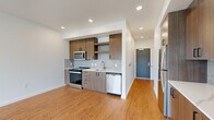 This well-appointed one-bedroom, one-bathroom residence offers a thoughtfully designed single-floor layout that maximizes both function and comfort. Warm hardwood-style flooring flows consistently throughout the space, complementing the bright, white walls and modern finishes.

The open-concept kitchen is a standout feature, equipped with stainless steel appliances including a refrigerator, electric range, microwave, and dishwasher. Medium-toned wood cabinetry with matte black hardware provides ample storage, while a light grey subway tile backsplash and white quartz countertops add a clean, contemporary aesthetic. The kitchen connects seamlessly to the living area, creating an inviting, functional common space.

The living room is bathed in natural light through expansive floor-to-ceiling windows and a sliding glass door, offering picturesque views of surrounding greenery and the neighborhood beyond. The bedroom continues this theme with tall windows framing lush tree-lined views and offering excellent natural light.

The bathroom features a full soaking tub with a tiled surround, complemented by a wood-toned vanity with a large mirror and modern fixtures. A dedicated closet provides convenient storage. The unit also includes an in-unit stacked washer and dryer, adding everyday practicality to this modern, light-filled residence.