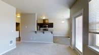 This single-floor residence offers a thoughtfully designed open-concept layout that seamlessly connects the kitchen, dining, and living areas. The kitchen is equipped with stainless steel appliances, including a refrigerator, microwave, and range, all framed by rich dark espresso cabinetry that provides ample storage. A granite-topped peninsula extends outward, offering bar-style seating and serving as a natural divider between the kitchen and the adjoining living space. A stylish pendant light hangs above, adding a warm, focused glow to the area. The living room is finished with plush wall-to-wall carpeting that adds comfort underfoot, while the kitchen and dining area transition to smooth hardwood-style flooring. Neutral warm-toned walls throughout create a cohesive and calming atmosphere. A large sliding glass door floods the living area with generous natural light and provides convenient access to the outdoors. The open flow of the layout makes the space feel airy and functional, ideal for both everyday living and entertaining. Clean lines, consistent finishes, and a well-considered design make this a comfortable and practical single-level home.