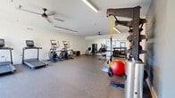 Located at 5816 Westpark Drive in Charlotte, NC, this fitness center offers a comprehensive workout environment designed to support a wide range of exercise routines. The space is laid out across a single open floor, providing generous room for movement and equipment use without feeling crowded.

The cardio zone features multiple treadmills and elliptical machines, all positioned to take advantage of the natural light streaming in through large windows and a glass door that opens to an outdoor area. Ceiling fans are mounted throughout, promoting airflow and comfort during workouts.

The strength training area is well-appointed, with a full rack of dumbbells, a weight bench, and cable/resistance machines. A TRX suspension training station adds functional fitness options, while a plyo box supports high-intensity interval training. Resistance bands and medicine balls, including a stability ball, round out the functional fitness equipment selection.

Durable rubber flooring spans the entire space, providing both safety and noise reduction. Full-length mirrors line one wall, enhancing the sense of openness while allowing users to monitor their form. Linear LED lighting fixtures illuminate the room evenly, complementing the natural light from multiple windows. The clean white and accent teal walls give the space a modern, energizing aesthetic well-suited to an active fitness environment.