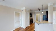 This single-floor residence offers a thoughtfully designed open layout that seamlessly connects the main living areas. Rich hardwood flooring flows through the central spaces, complemented by plush carpeting in the adjacent bedroom, creating a warm and inviting atmosphere throughout. Crown molding adds an elegant finishing touch to every room, enhancing the sense of refinement.

The kitchen is a standout feature, equipped with dark cabinetry, stainless steel appliances, and granite countertops that extend to a peninsula with an overhang — ideal for casual dining or entertaining. A stylish pendant light fixture illuminates the countertop area, while a track lighting system provides additional task lighting. A louvered door provides access to a closet or utility area nearby, adding functional storage to the space.

Neutral, warm-toned walls throughout the residence create a versatile backdrop that suits a variety of interior styles. Doorways lead to multiple rooms, including what appears to be a bedroom and an additional room — possibly a bathroom or laundry area — each accessible from the central hallway. Ample natural and artificial lighting ensures the space feels bright and welcoming. The overall design balances practicality with understated elegance.