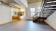 Located at 221 N Eighth St in downtown St. Louis, this two-floor urban loft blends industrial character with modern finishes. The main floor offers an expansive open-plan layout with large-format tile flooring, dramatic soaring ceilings, and exposed silver ductwork that nods to the building's industrial heritage. Natural light streams in through generous windows, offering views of the surrounding cityscape. A sleek steel staircase with wire-mesh railings connects the two levels, serving as a striking architectural focal point.

The well-appointed kitchen features warm wood cabinetry, granite countertops, a glass tile backsplash, stainless steel appliances including a refrigerator, range, microwave, and dishwasher, as well as a center island and stylish pendant lighting. A full bathroom on the main level includes light wood vanity cabinetry and tile flooring.

The upper loft level retains the building's raw character with original exposed concrete beams and columns, and is finished with plush carpeting. This level also includes a full bathroom with a soaking tub and shower combination, and a spacious walk-in closet outfitted with wire shelving. Together, the two floors provide a functional and distinctive urban living environment in the heart of downtown St. Louis.