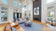 Located at 1000 Shadowood Pkwy SE in Atlanta, GA, this elegantly designed single-floor space serves as a welcoming community hub, blending classic architectural details with contemporary furnishings. The entry foyer greets visitors with bold double glass doors framed in crisp white millwork, transom windows, and warm natural wood flooring that flows seamlessly throughout the entire space.

The main lounge area is defined by dramatic double-height ceilings, coffered detailing, and an eye-catching modern chandelier. A floor-to-ceiling dark stone fireplace serves as the room's focal point, adorned with large-scale abstract artwork that adds a curated, gallery-like quality. Plush seating, including a neutral sectional sofa and rich cognac leather chairs, creates an inviting atmosphere for relaxation or conversation.

Adjacent to the lounge, a cozy nook with a round pedestal table and modern chairs offers garden views through large windows, bathing the area in natural light. The leasing or service counter features a long white quartz surface accented by velvet blue chairs and pendant lighting, set against a striking dark shiplap feature wall. Throughout the space, white walls, abundant windows, and lush greenery visible from every angle contribute to a bright, airy, and refined ambiance.