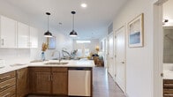 This thoughtfully designed one-bedroom, one-bathroom unit in Clarksville, Indiana offers a functional and modern single-floor layout. The open-concept kitchen and living area serves as the heart of the space, where the kitchen features a two-toned cabinetry design—warm wood lower cabinets paired with crisp white uppers—topped with light countertops. Stainless steel appliances, including a refrigerator, range, microwave, and dishwasher, provide a polished, contemporary feel. A peninsula with pendant lighting doubles as a prep and dining area, flowing seamlessly into the living room. The living room benefits from natural light through a transom window above French doors, which open to an outdoor space. Light wood-style flooring runs throughout the main living areas, contributing to the bright, airy atmosphere. The bedroom is a comfortable retreat, featuring carpet flooring, a ceiling fan, large windows that invite natural light and outdoor views, and direct access to a dedicated closet with built-in shelving. The bathroom is finished with wood-toned cabinetry, a single vanity with a white countertop, and a tiled tub-shower combination, maintaining the cohesive modern aesthetic found throughout the unit.