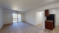 This single-floor unit offers a straightforward, functional layout designed for comfortable everyday living. The living area is generously proportioned, finished with neutral-toned wall-to-wall carpeting and white walls that create a clean, bright atmosphere. Vertical blinds cover a sliding glass door that opens to an outdoor balcony, allowing natural light to filter into the space and providing views of surrounding greenery.

The kitchen is positioned adjacent to the living area and transitions to light wood-style vinyl flooring. It features rich dark wood cabinetry, granite-style countertops, and stainless steel appliances including a gas range, refrigerator, and dishwasher, all accented by an overhead range hood. A ceiling fan is installed above, improving ventilation and airflow throughout the combined kitchen and living space.

The bedrooms are carpeted and well-sized, each offering ample wall space for furniture placement. One bedroom includes a vertical blind-covered window that admits natural light. The bathroom is outfitted with wood-style flooring, a dark wood vanity with a granite-style countertop, a wall-mounted mirror, vanity lighting, and a full bathtub with shower. The overall aesthetic throughout the unit is neutral and move-in ready.