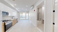 Located at 40 Lembeck Avenue in Jersey City, NJ, this thoughtfully designed two-bedroom, two-bathroom unit offers a clean, modern aesthetic across a single floor. The layout is efficiently organized with two hallways connecting the main living areas, providing a smooth flow throughout the space.

The kitchen is a standout feature, showcasing a contemporary design with a combination of warm wood lower cabinets and high-gloss white upper cabinetry. A vertically stacked tile backsplash, white quartz countertops, a matte black faucet, and a full suite of stainless steel appliances — including a gas range, microwave, refrigerator, and dishwasher — complete this functional and stylish space.

Both bedrooms are finished with light-toned herringbone hardwood flooring and crisp white walls. The primary bedroom benefits from a large window that invites natural light and offers views of the surrounding neighborhood. Each room is equipped with a wall-mounted mini-split HVAC unit for individual climate control.

The two bathrooms are distinctly finished. One features a glass-enclosed walk-in shower, a warm wood vanity with matte black fixtures, and light tile flooring. The second bathroom includes a full soaking tub with a tiled surround and a wall-mounted sink. Both bathrooms maintain a clean, minimalist look consistent with the overall design of the unit.