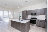 Located in American Fork, Utah, this modern 3-bedroom, 1-bathroom residence offers a thoughtfully designed single-floor layout with contemporary finishes throughout. The open-concept living and kitchen area serves as the heart of the home, featuring light wood-tone cabinetry, crisp white quartz countertops, a central island with an undermount sink and matte black faucet, and a full suite of stainless steel appliances including a refrigerator, range, and microwave. Light hardwood-style flooring runs throughout the main living areas, complementing the bright, neutral palette. A sliding glass door fills the living space with natural light and provides access to an outdoor balcony with neighborhood views. The bedrooms are carpeted and well-lit with large windows that invite ample sunlight; the spacious primary bedroom includes a ceiling fan. The shared bathroom is well-appointed with a dual-sink vanity featuring wood cabinetry and quartz surfaces, framed mirrors, and a tub-shower combination. A walk-in closet with built-in shelving and hanging rods provides generous storage. A dedicated utility room and additional closet space round out the practical features of this clean, move-in-ready home.