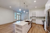 Located at 333 W 24th St in Houston, TX, this well-appointed 2-bedroom, 2-bathroom single-story home showcases a thoughtfully designed open-concept floor plan with modern finishes throughout. The kitchen serves as the centerpiece of the living area, featuring a large island with a stainless steel farmhouse sink, crisp white shaker cabinetry, quartz countertops, a subtle gray tile backsplash, and stainless steel appliances including a refrigerator, range, and microwave. Pendant lighting above the island and recessed ceiling lights enhance the bright, airy atmosphere. The kitchen flows seamlessly into the living area, which is bathed in natural light through large windows and French doors that open to an outdoor balcony. Warm-toned hardwood-style flooring runs throughout the main living spaces and bedrooms. The primary bedroom offers a comfortable layout with a ceiling fan and a well-organized walk-in closet featuring built-in shelving and hanging rods. The second bedroom is bright and open, with a large window and its own walk-in closet with corner shelving. Both bathrooms are finished with marble-look tile, white vanities with quartz countertops, and elegant brass-toned fixtures, with one bathroom featuring a lighted vanity mirror and a tub-shower combination.