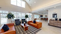 Located at 1649 SR-12 N in Ashland City, Tennessee, this single-floor community clubhouse is designed to offer a well-appointed gathering space with distinct functional zones flowing seamlessly from one to the next. The entrance foyer makes a strong first impression with soaring vaulted ceilings, an arched dark-wood double door, and dramatic clerestory windows that flood the space with natural light. A cowhide rug and sculptural accent table anchor the entry, adjacent to a dedicated office or leasing area.

The main lounge area features the standout vaulted ceiling with exposed ridge lines and large windows on multiple walls, creating an open, airy atmosphere. Cognac leather sofas, navy accent chairs, and a bold black-and-white plaid area rug provide comfortable, stylish seating. Light wood-look tile flooring extends throughout the entire space, maintaining visual continuity.

Toward the rear, a wet bar area is finished with dark granite countertops, stone veneer detailing, white cabinetry, and a wall-mounted television. High-top tables and leather barstools furnish this social zone. An adjacent game room offers additional high-top seating, framed artwork, and a shuffleboard table, making it a versatile recreational space ideal for community gatherings.