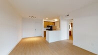 This single-floor residence offers a clean, modern design highlighted by light hardwood-style flooring that runs throughout the main living areas, creating a bright and cohesive atmosphere. The open-plan layout seamlessly connects the living area to the kitchen, which features warm wood cabinetry with gold-tone hardware, dark countertops, a white peninsula with a built-in sink, and a full suite of stainless steel appliances including a gas range, microwave, and refrigerator. The kitchen's galley-style configuration provides ample counter and storage space, making it both practical and visually appealing. The living area is generously proportioned and illuminated by a track lighting fixture, with a sliding glass door leading to an outdoor area. The bedroom is a calm, neutral retreat finished with plush carpeting, white walls, and a closet with bifold doors. The bathroom is elegantly appointed with large-format marble-look tile in the shower and tub surround, warm wood cabinetry, a white quartz vanity countertop, an under-mount sink with a brushed nickel faucet, and a backlit mirror. Together, the spaces deliver a cohesive, contemporary living environment with quality finishes throughout.