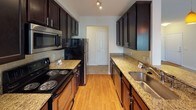 This single-story space is designed with a neutral, cohesive palette of warm beige tones throughout, creating a calm and consistent aesthetic. Plush wall-to-wall carpeting runs through the main living areas, bedrooms, and hallway, while wood-look flooring adds warmth to the kitchen and bathrooms.

The galley-style kitchen is well-appointed with dark espresso cabinetry, granite-look countertops, a tile backsplash, stainless steel appliances, and track lighting overhead. It connects to a dining area featuring crown molding, a ceiling fan, and direct outdoor access via a glass-paneled door, alongside a large window that invites natural light.

The carpeted living area is generously proportioned, offering multiple windows with blinds and a ceiling fan. A carpeted hallway with wall sconce lighting connects the bedrooms, each equipped with ceiling fans and windows providing outdoor views. One bedroom features a recessed nook, adding additional functional space.

Both bathrooms share a consistent design: dark vanity cabinetry, white countertops, wood-look flooring, large mirrors, and a tub-shower combination. Crown molding details appear in select rooms, contributing to a refined finish throughout the space.