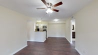 This single-story residence is designed with a practical and comfortable open-concept layout. The main living area is expansive and airy, featuring rich dark hardwood-style flooring that flows consistently throughout the unit. A ceiling fan with an integrated light fixture anchors the living space, while a peninsula-style kitchen with pendant lighting, white cabinetry, granite-look countertops, and stainless steel appliances connects seamlessly to the living area. The kitchen is galley-style on its interior side, offering ample cabinetry and counter space on both sides, along with a stainless steel sink and black appliances including a refrigerator and range.

The bedrooms are generously sized, each equipped with a ceiling fan and windows that invite natural light and outdoor views of surrounding greenery. One bedroom benefits from sliding glass doors that open to an outdoor patio area. The bathrooms feature tile flooring, dark wood vanities with light stone-topped counters, framed mirrors, and tiled tub-shower combinations. A dedicated in-unit laundry room accommodates a full-size washer and dryer, adding everyday convenience to the overall functional design of the space.