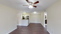 This single-story residence is designed with a practical and comfortable open-concept layout. The main living area is expansive and airy, featuring rich dark hardwood-style flooring that flows consistently throughout the unit. A ceiling fan with an integrated light fixture anchors the living space, while a peninsula-style kitchen with pendant lighting, white cabinetry, granite-look countertops, and stainless steel appliances connects seamlessly to the living area. The kitchen is galley-style on its interior side, offering ample cabinetry and counter space on both sides, along with a stainless steel sink and black appliances including a refrigerator and range.

The bedrooms are generously sized, each equipped with a ceiling fan and windows that invite natural light and outdoor views of surrounding greenery. One bedroom benefits from sliding glass doors that open to an outdoor patio area. The bathrooms feature tile flooring, dark wood vanities with light stone-topped counters, framed mirrors, and tiled tub-shower combinations. A dedicated in-unit laundry room accommodates a full-size washer and dryer, adding everyday convenience to the overall functional design of the space.