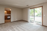This single-floor unit offers a practical and straightforward layout designed for comfortable everyday living. The spacious living area is finished with light-toned carpeting and neutral walls, with sliding glass doors that invite natural light and provide direct access to a private balcony overlooking greenery. A separate, similarly carpeted room features a distinctive bay window arrangement, flooding the space with additional natural light and creating an airy atmosphere.

The kitchen is equipped with warm-toned wooden cabinetry offering generous upper and lower storage, laminate countertops, and tile flooring. Appliances include an electric range, dishwasher, and refrigerator, providing a fully functional cooking space. A range hood is positioned above the cooktop for ventilation.

The bedroom is well-proportioned with plush carpeting and access to a large walk-in closet outfitted with dual hanging rods and shelving on both sides, offering substantial storage capacity. The full bathroom features a tiled tub-and-shower combination, a vanity with storage, and a window that provides natural ventilation. Throughout the unit, dark wood baseboards and trim provide a consistent design detail that grounds the neutral color palette.