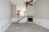This home offers a thoughtfully designed layout across a single level, with additional upper-floor access via a staircase featuring wood balusters and a classic railing. The living room serves as a central gathering space, distinguished by tall walls, plush neutral carpeting, white wainscoting panels, a ceiling fan, and a stone-surround fireplace with a wood mantel that anchors the room with warmth and character.

The kitchen is well-equipped, featuring warm oak cabinetry extending to the ceiling, dark granite-style countertops, tile flooring, and black appliances including a range, microwave, and dishwasher. A window above the sink brings in natural light, and a nearby exterior door provides convenient access.

The bedrooms are carpeted and finished in neutral tones, each with ceiling fans or recessed lighting. One bedroom includes a walk-in closet, while others feature standard closets and windows. Two full bathrooms serve the home: one includes a single-sink oak vanity, tile flooring, and a tub/shower combo, while the second offers a framed glass walk-in shower, vanity, and tile flooring. Throughout, the home maintains a clean, neutral aesthetic with consistent finishes.