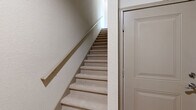 This three-floor residence in Fredericksburg, Virginia offers a well-organized layout across its three levels, totaling a comfortable and functional living space. The entry level provides a welcoming hallway that leads to the carpeted staircase connecting all floors. The main living level serves as the heart of the home, featuring an open-concept dining room, kitchen, and living room. The kitchen is appointed with white shaker cabinetry, a mosaic tile backsplash, stainless steel appliances including a refrigerator, range, and dishwasher, and warm hardwood flooring that extends throughout the living and dining areas. The living room is bright and airy, with multiple windows, a ceiling fan, and glass doors opening to a private balcony. A full bathroom with a tub-shower combination and wood-look flooring is also found on this level. The upper floor houses both bedrooms, each carpeted and filled with natural light from multiple windows. The primary bedroom features soaring ceilings and a dedicated walk-in closet with wire shelving. A dedicated in-unit laundry room with a full-size washer and dryer adds everyday convenience. Three full bathrooms, two hallways, and a pantry round out this well-appointed multi-floor home.