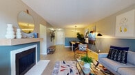 Located at 2570 S Dayton Way in Denver, Colorado, this thoughtfully designed single-floor residence offers a comfortable and contemporary living experience. The open-concept living area is a welcoming focal point, highlighted by a tiled fireplace, light wood flooring, and a bold teal accent wall adorned with curated artwork. Large sliding glass doors flood the space with natural light and provide direct access to a private balcony overlooking lush greenery. The adjacent dining area features a modern linear pendant light and continues the cohesive teal color palette, creating a seamless flow throughout the main living space. The galley-style kitchen is efficiently laid out with dark cabinetry, stainless steel appliances, and ample counter space. The primary bedroom is generously sized, offering balcony access, a walk-in closet, and room for a full furniture suite. A second bedroom provides comfortable accommodations with its own closet. The primary bathroom features an extended vanity with dark cabinetry, a large mirror, and bright overhead lighting, while a second full bathroom includes a tiled shower-tub combination. Light wood-style flooring runs throughout, tying the entire residence together with a warm and modern aesthetic.