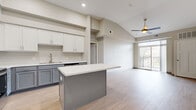 This well-designed single-floor unit offers 2 bedrooms and 1 bathroom within a thoughtfully laid-out floor plan. The open-concept kitchen and living area serves as the heart of the unit, featuring vaulted ceilings that enhance the sense of spaciousness. The kitchen is equipped with a two-tone cabinet design — white upper cabinets paired with gray lower cabinets — complemented by a white countertop, stainless steel appliances including a full-size refrigerator, and a central island providing additional workspace and storage. Light wood-look flooring runs throughout the main living area, adding warmth and continuity.

The living area benefits from abundant natural light through a sliding glass door that opens to a private balcony with outdoor views. A ceiling fan overhead adds comfort and functionality. Both bedrooms are carpeted, providing a softer feel underfoot, and one bedroom includes a sliding-door closet with wire shelving for organized storage.

The bathroom features a gray vanity with a white countertop, a framed mirror, and light wood-look flooring consistent with the main living areas. A dedicated laundry area accommodates a full-size washer and dryer, adding everyday convenience to this efficiently designed unit.