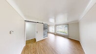 Located at 5965 Evergreen Road in Dearborn Heights, MI, this 2-bedroom, 1-bathroom unit offers a clean, modern aesthetic across its single-floor layout. Light wood laminate flooring runs throughout, creating a bright and cohesive feel in every room.

The living room is a comfortable, open space filled with natural light from a large window dressed with vertical blinds, offering views of the surrounding neighborhood. A standout design element is the sliding barn door with a reclaimed wood accent wall, adding a rustic-modern touch to the living area.

The kitchen is efficiently laid out with white cabinetry, dark granite countertops, and a full suite of stainless steel appliances including a refrigerator, gas range, and over-the-range microwave. Light wood flooring continues seamlessly into this space.

The primary bedroom is generously sized with a double-door closet and direct access to the hallway. The second bedroom features a window with vertical blinds and a wall-mounted air conditioning unit, providing independent climate control. Both bedrooms maintain the same light, neutral palette found throughout the unit.

The bathroom is neatly finished with large-format grey stone-look tile on both the floors and walls, a soaking tub with a handheld showerhead, a white vanity, and a dark granite countertop, tying together the unit's consistent design language.