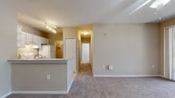 This single-story, 2-bedroom, 1-bathroom residence offers a practical and comfortable layout designed for efficient everyday living. The open-concept living and dining area is finished with plush carpeting, neutral warm-toned walls, and a ceiling fan, creating a welcoming atmosphere. A sliding glass door leads to a private balcony that overlooks lush greenery, bringing natural light deep into the living space.

The kitchen is positioned at the heart of the home, featuring a peninsula with a countertop overhang that opens to the living area. White cabinetry with ample storage, a tile backsplash laid in a diagonal pattern, light countertops, and white appliances — including a range, dishwasher, and refrigerator — complete the well-equipped space. Light tile flooring runs throughout the kitchen.

Both bedrooms are carpeted and fitted with ceiling fans. Each room benefits from windows that invite natural light and offer views of the surrounding landscape. The primary bedroom includes access to a spacious walk-in closet outfitted with multi-tier wire shelving for generous storage. A built-in shelving nook in the living area provides additional display and storage space.

The bathroom features a full tub-shower combination with tile surround, a vanity with granite-style countertops, and tile flooring. A dedicated utility room and an additional closet round out the storage options throughout this thoughtfully arranged home.