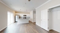 This single-floor residence offers a thoughtfully designed open-concept layout that seamlessly connects the living area to the kitchen. The living space features warm hardwood-style flooring, neutral beige walls, crown molding, and a ceiling fan with light fixture, creating a comfortable and inviting atmosphere. Large windows and a sliding glass door allow natural light to fill the room while providing views of the outdoors.

The kitchen is a standout feature, showcasing white cabinetry, a tile backsplash, granite countertops, and stainless steel appliances including a refrigerator, range, and built-in microwave. A central island with an integrated sink and pendant lighting above adds both functionality and visual appeal.

The bedrooms are generously sized with the same hardwood-style flooring, crown molding, and ceiling fans. One bedroom includes a walk-in closet outfitted with wire shelving, offering ample storage. An additional bedroom provides access to a hallway bathroom and utility area. The bathroom features a clean, all-white walk-in shower with chrome fixtures.

Additional highlights include a dedicated electrical panel room and consistent use of crisp white trim and neutral tones throughout, giving the entire space a fresh, move-in-ready feel.