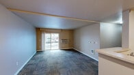 Located in Airway Heights, WA, this two-bedroom, two-bathroom residence offers a functional and comfortable single-floor layout. The combined kitchen and living area forms the heart of the home, where patterned carpet flows throughout the living space and a sliding glass door opens to a private balcony, filling the room with natural light. The kitchen is well-appointed with warm wood cabinetry, light countertops, a double-basin stainless steel sink, black appliances including a refrigerator and range, and tile flooring. A dedicated pantry provides additional storage convenience. Both bedrooms are carpeted and finished in neutral tones, with the primary bedroom offering a generous footprint and ample closet space — three closets are distributed throughout the unit. The bathrooms are finished with tile flooring, wood-toned vanities, and a shower-tub combo. Baseboard heating is present in the bedrooms, while wall-mounted HVAC units serve the main living areas. Clean white trim and neutral warm-toned walls create a consistent, move-in-ready aesthetic throughout the entire residence.